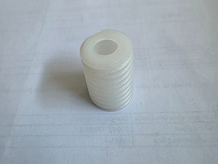 Beli plastični deo sa spoljnim navojem, na papiru.