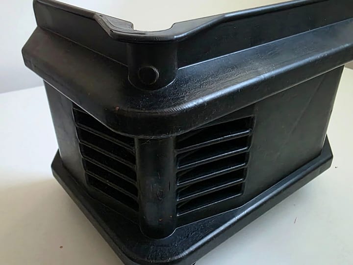 Crno plastično kućište sa rebrastom rešetkom i ivicom za montažu.