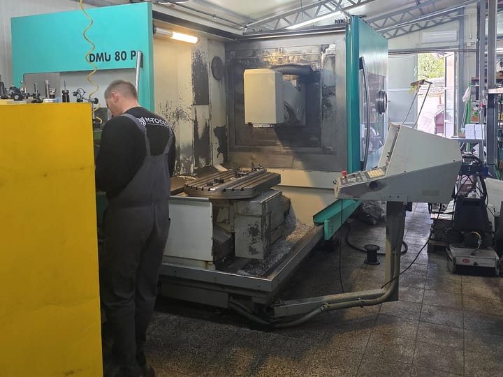 CNC glodalica DMU 80 P sa otvorenim radnim prostorom i okruglim stolom; operater u majici M-TOOLS radi pored mašine, desno je upravljački pult.