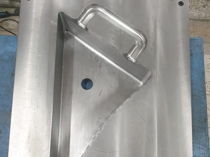 Aluminijumska polovina kalupa sa gnezdom za trouglastu posudu sa drškom, na plavoj ploči.