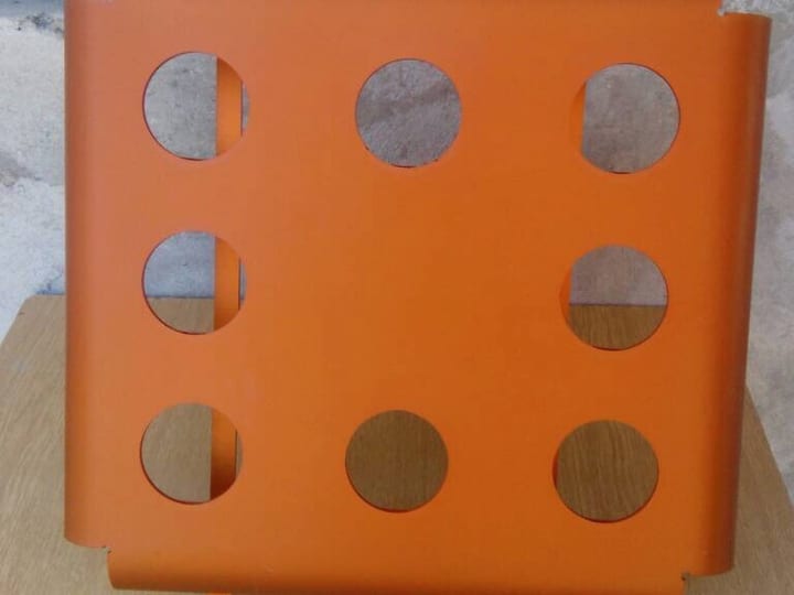 Narandžasti savijeni limeni panel sa kružnim otvorima, okačen.