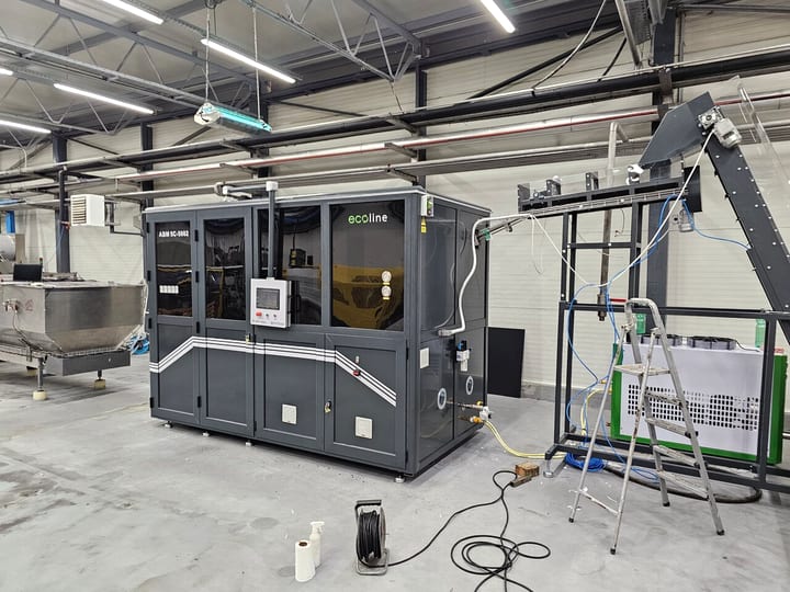 Automatska PET duvaljka u tamnosivom kućištu sa transporterom predformi, u proizvodnoj hali (2023).
