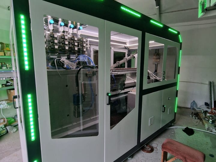 Automatska PET duvaljka u belom kućištu sa crnim ramom i zelenim LED trakama, u hali (2025).