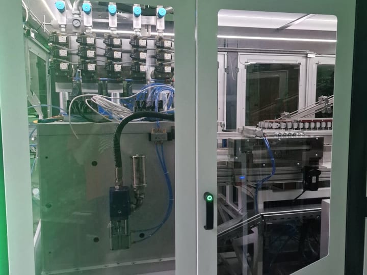 Automatska PET duvaljka sa zelenim LED trakama; kroz staklena vrata vidi se pneumatika i transporter (2025).